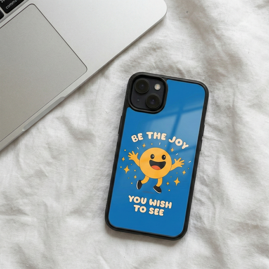 Be The Joy You Wish To See blue glass iPhone case by Spiritual Kalakaar placed beside laptop on soft fabric surface
