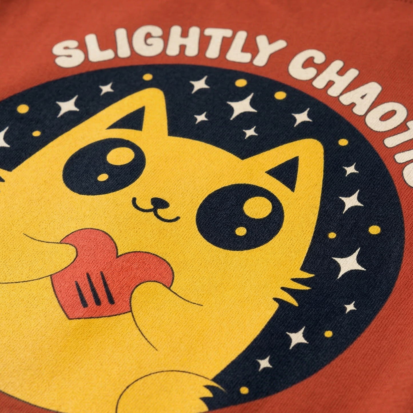 Close-up of cute yellow cat holding heart with “Slightly Chaotic Always Kind” illustration