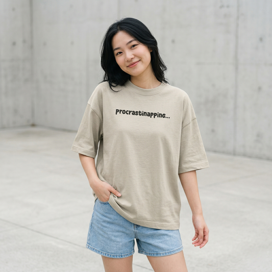 Woman wearing beige oversized t-shirt with procrastinapping text relaxed playful aesthetic