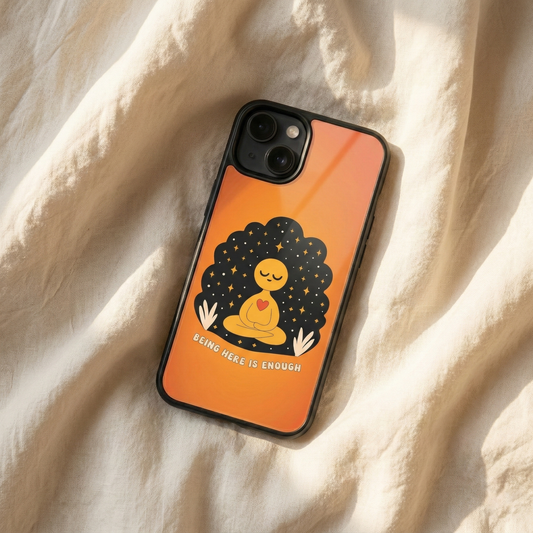 Being Here Is Enough orange glass iPhone case by Spiritual Kalakaar with meditation artwork placed on soft fabric in warm sunlight