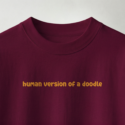 Close-up of “human version of a doodle” text on burgundy oversized t-shirt