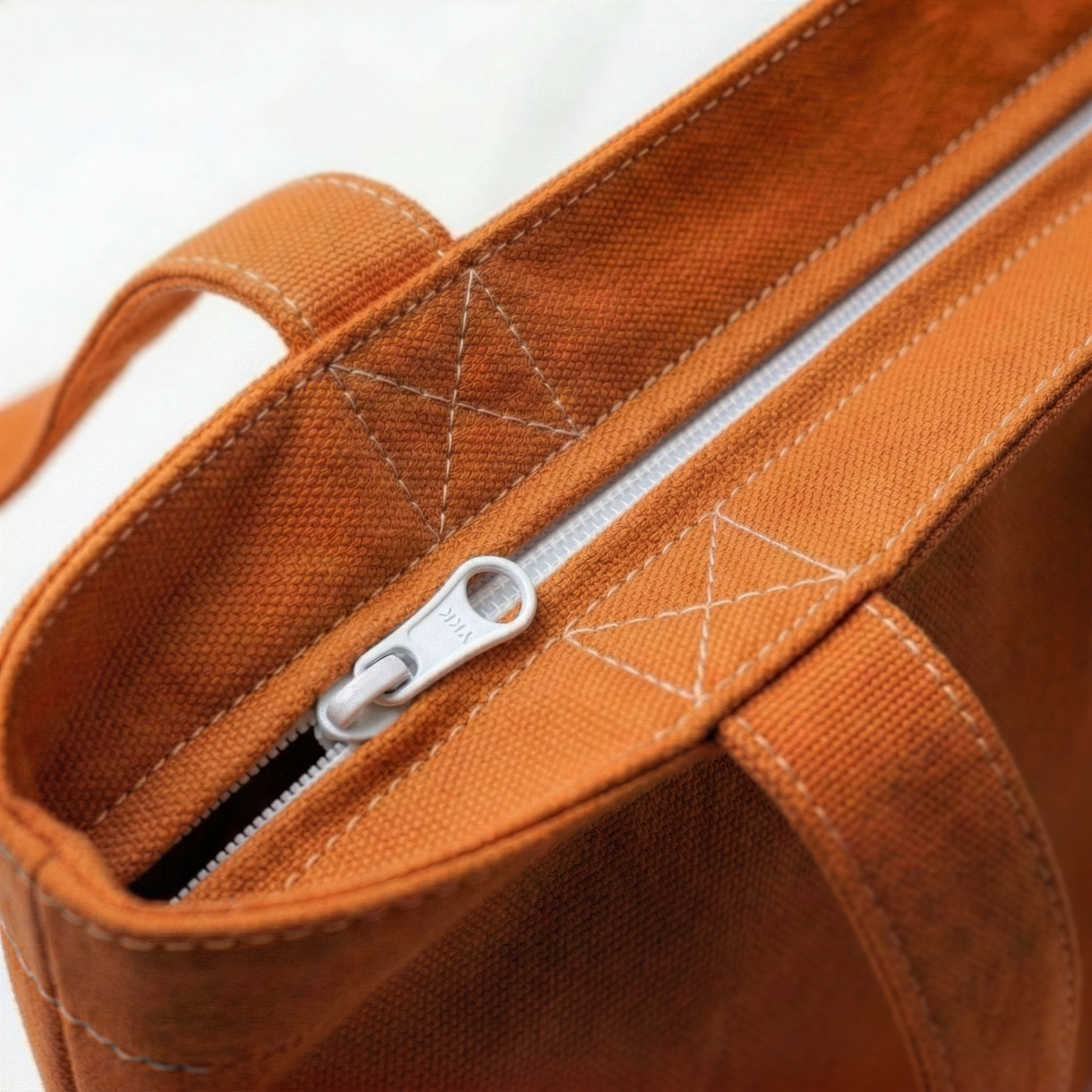 Close-up of orange canvas tote bag showing secure zip closure and reinforced stitching detail