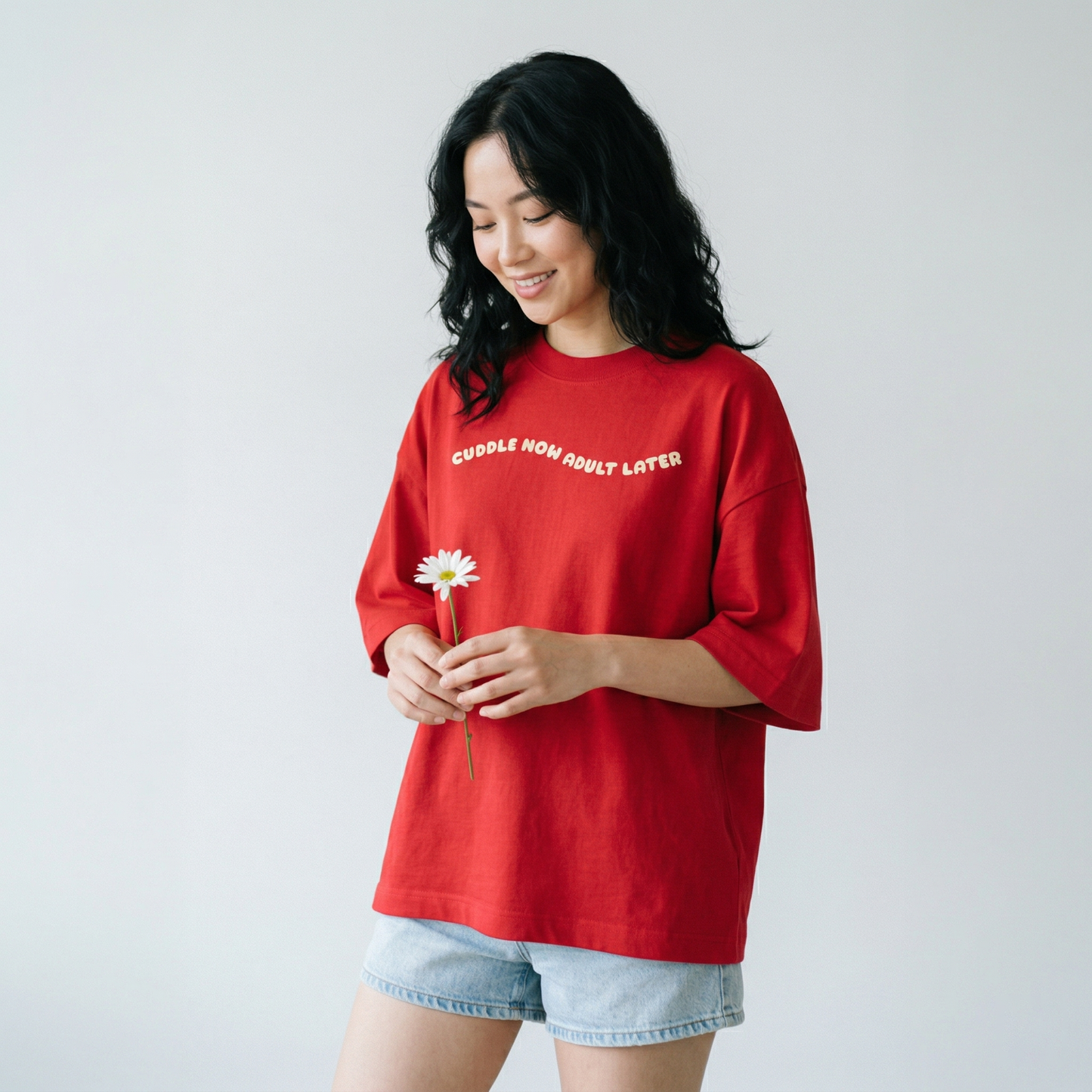 Woman wearing red oversized t-shirt with cute relatable text holding a flower